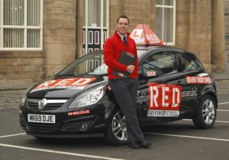 RED driving instructor leaning on RED car