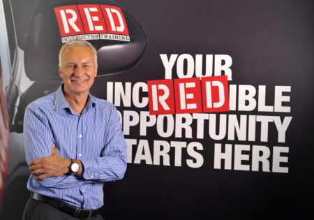 Middle aged man smiling infront of RED instructor training background