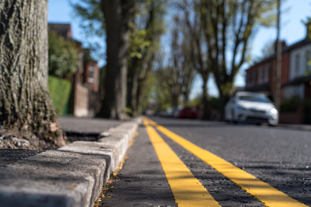 Close up of double yellow lines (meaning, no parking at any time) at the curb of a tree lined residential urban street, Belfast, Northern Ireland.